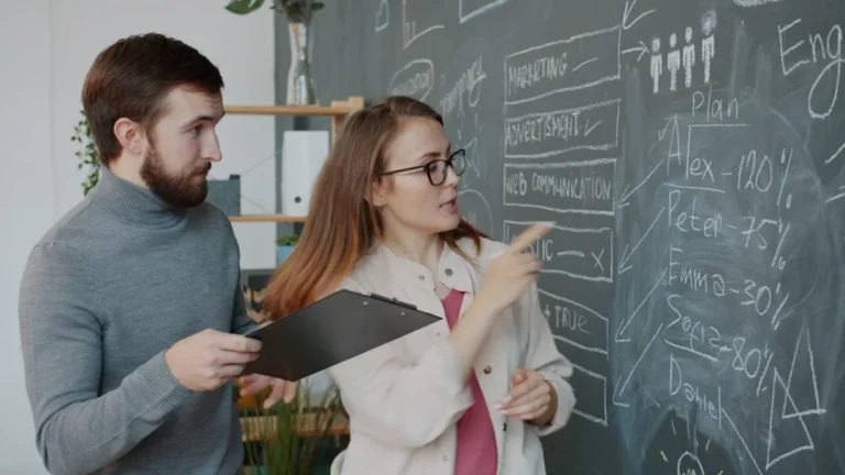 Two colleagues discussing a diagram on a chalkboard.