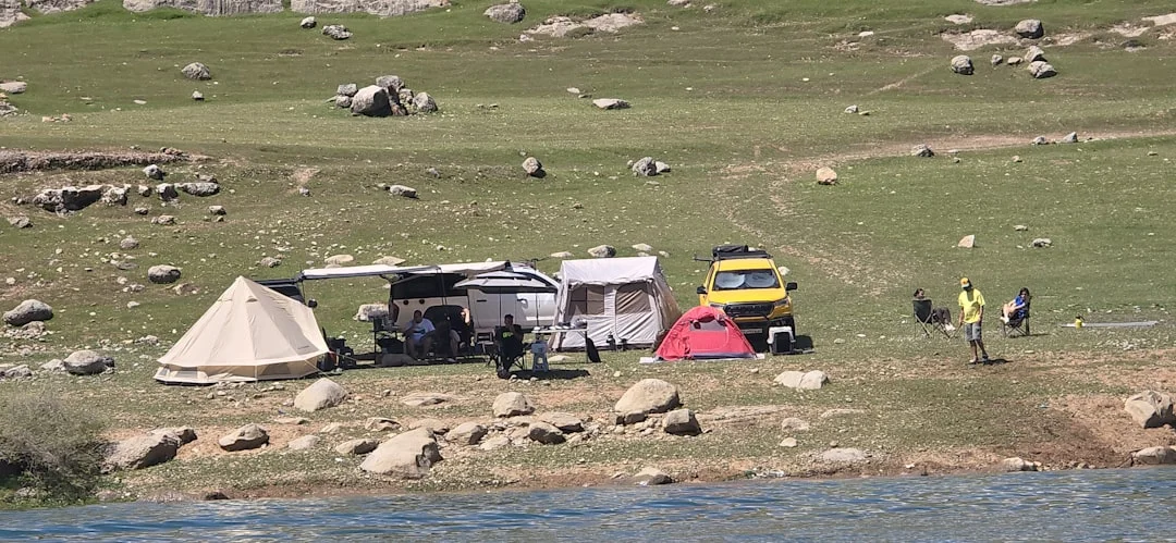 Campground with tents and vehicles by the water.