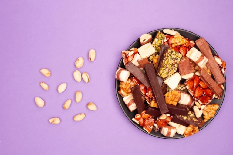 A plate of assorted candies and pistachios on purple background