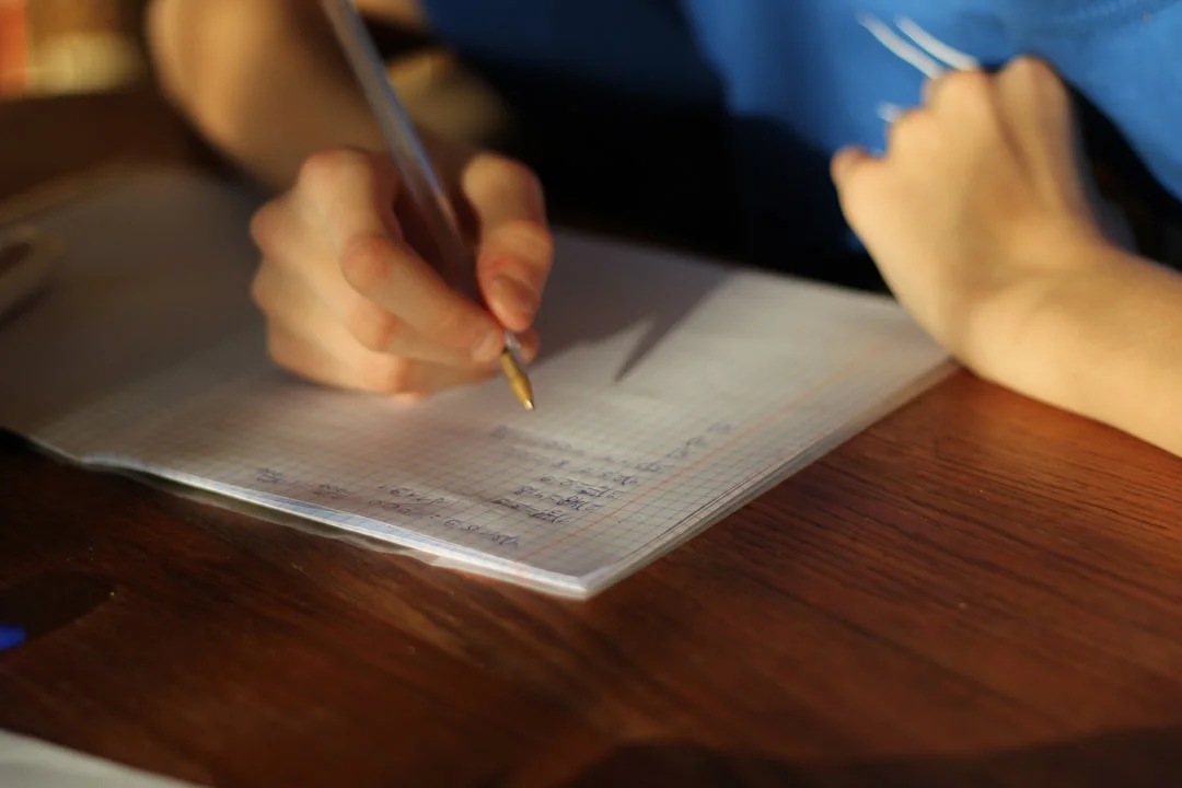 A person sitting at a table writing on a piece of paper