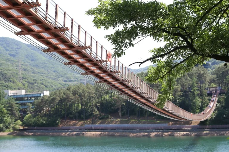 A suspension bridge spans a lake surrounded by green mountains.