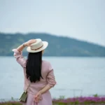 Woman in hat looking at a serene lake landscape.