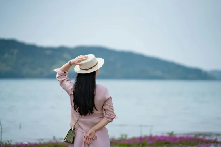 Woman in hat looking at a serene lake landscape.