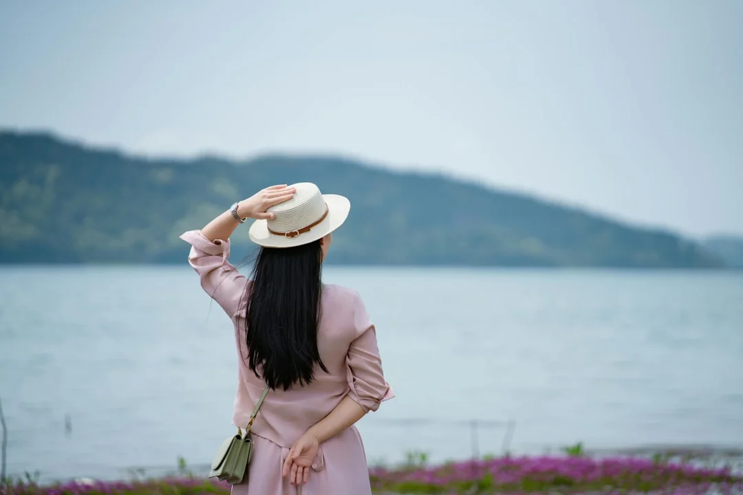 Woman in hat looking at a serene lake landscape.