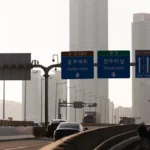 Road signs on a highway with city buildings.