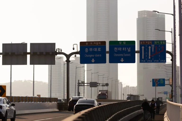 Road signs on a highway with city buildings.