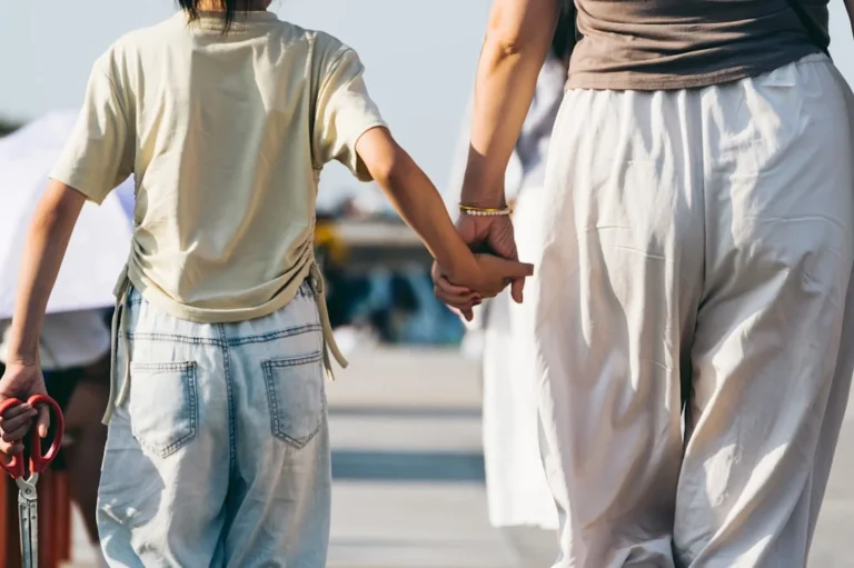 A mother and child hold hands while walking.