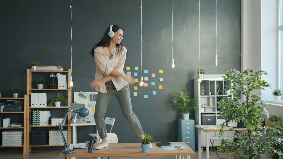 Woman dancing on desk wearing headphones in office
