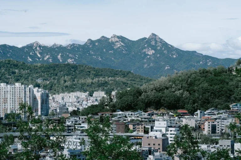 white and brown concrete buildings near green mountain under white sky during daytime